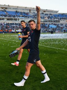 two soccer players are walking on the field with their arms in the air and one is holding a ball