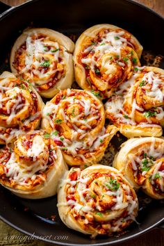 a pan filled with pizza rolls covered in cheese and sauce on top of a wooden table