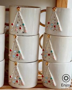 white cups with christmas trees on them stacked next to each other in front of a wooden shelf