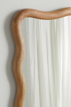 a wooden mirror hanging on the wall next to a white drapes covered window with curtains behind it