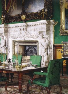 a dining room with green chairs and a fireplace in the center, surrounded by ornate paintings