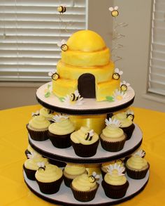 a three tiered cake with cupcakes on it and bees around the top