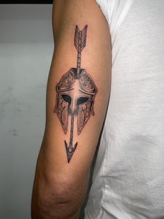 a man's arm with a spartan helmet and an arrow tattoo on the left upper arm