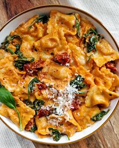 a white bowl filled with pasta and spinach on top of a wooden table next to a napkin