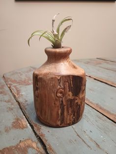 a wooden vase with a plant in it on top of a blue wood table next to a wall