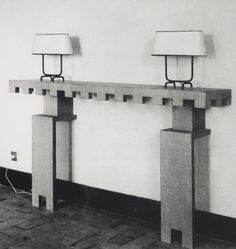 two lamps sitting on top of a wooden table next to a white wall and brick floor