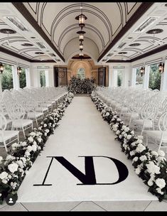 an indoor wedding venue with white chairs and flowers on the aisle, decorated with monogrammed letters