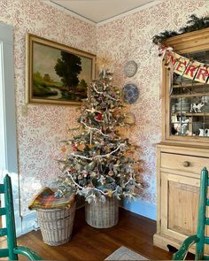 a decorated christmas tree in a living room next to two chairs and a china cabinet