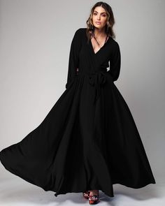 This 70s inspired maxi dress features a seductive cross front V-shaped surplice neckline, guaranteed to grab attention wherever you go. The elasticized waist ensures a fit across various sizes, complemented by an attached self-tying belt. The cuffed bell sleeves add a hint of vintage glamour. The opaque fabric has a butter-soft hand with a deep jet black hue. The full, sweeping maxi skirt is partially lined for comfort and style.  ** Based on the settings of your display, colors may vary slightl Circle Maxi Skirt, Retro Glamour, Black Slip Dress, Fashion District, Medium Dress, Mid Length Skirts, 70s Inspired, Black Slip Ons, Lily Pads