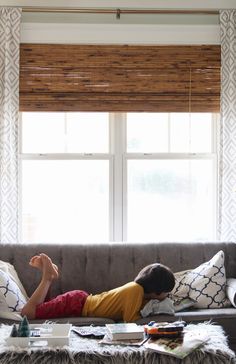 a woman laying on top of a couch in front of a window next to a coffee table