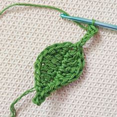 a green crochet piece with a blue needle