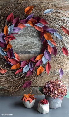 a wreath made out of paper flowers and twigs on a table next to two small pots