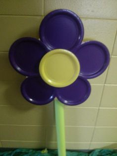 a purple flower shaped object sitting on top of a green pole in front of a tiled wall