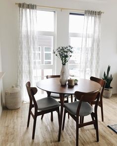 a dining room table with chairs and a vase on it in front of a window