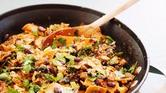 a skillet filled with lots of food on top of a table next to a wooden spoon