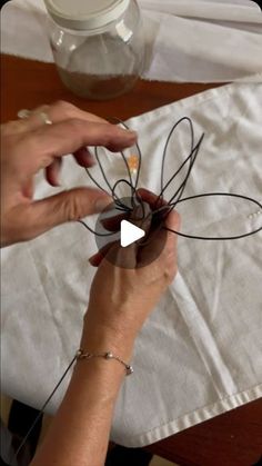 two hands are working on something with wire and paper in front of them, while another hand is holding the string