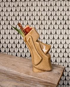 a ceramic vase sitting on top of a wooden table in front of a wallpaper