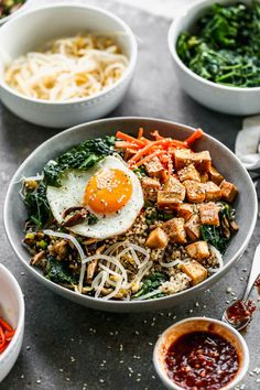 a bowl filled with noodles, tofu and vegetables next to bowls of sauces