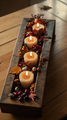 some candles are sitting in a long wooden tray with leaves and berries on the table