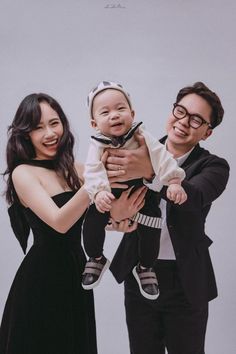 a man holding a baby while standing next to two women in black dresses and tuxedos