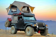 a jeep with an awning on top of it parked in the desert at sunset