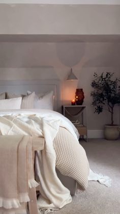 a bed with white sheets and pillows in a bedroom next to a plant on the floor