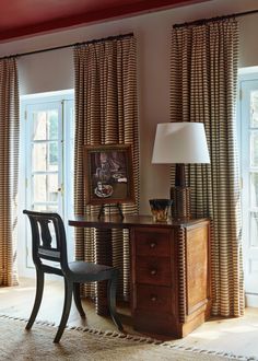 a chair and desk in front of two windows with curtains on the window sill