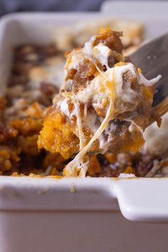 a spoon full of food in a casserole dish with meat and cheese on top