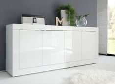 a white cabinet with drawers and doors in a living room next to a vase filled with flowers