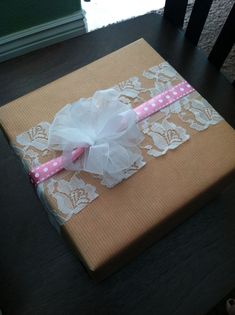 a present wrapped in brown paper with white lace and pink polka dots on it sitting on top of a wooden table