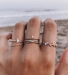 a woman's hand with three rings on it and the ocean in the background