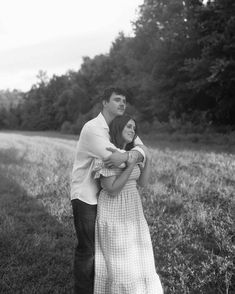 black and white photograph of a couple embracing in the grass near a road with trees