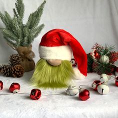 a stuffed toy with green hair wearing a santa hat next to christmas decorations and pine cones