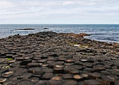 a large rock formation near the ocean with water in the background and clouds in the sky