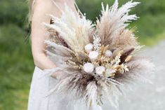 a woman in a white dress holding a bouquet of dried flowers and feathers on her arm