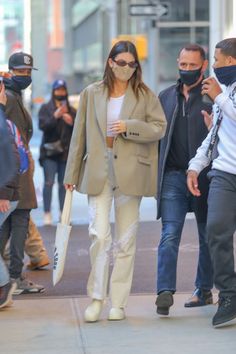 a woman wearing a face mask walks down the street with her hand in her pocket