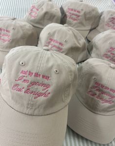 several baseball caps with pink writing on them sitting on a striped cloth covered tablecloth