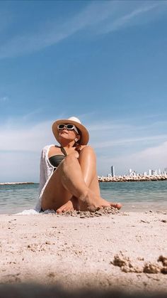 a woman sitting on the beach wearing a hat and sunglasses