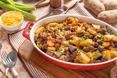 a casserole dish with meat, potatoes and green onions on a wooden cutting board