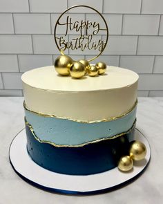 a blue and white birthday cake with gold decorations on the top is sitting on a plate