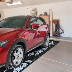 a red car parked in a garage with snow all over the floor and on the ground