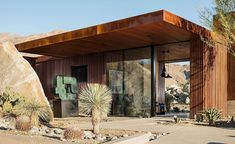 a desert house with large rocks and cactus in the foreground, on a sunny day