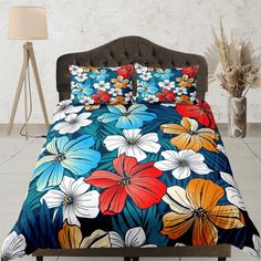 a bed with colorful flowers on it in a room next to a lamp and vase