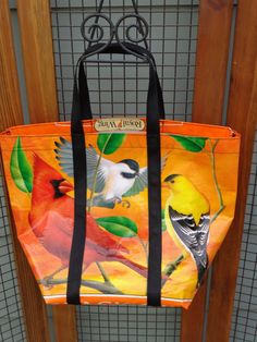 an orange purse with birds on it hanging from a door handle and metal grate