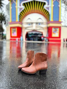 a pair of brown cowboy boots sitting on top of a wet floor next to a carnival ride