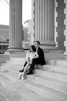 a man and woman sitting on the steps of a building with columns in the background