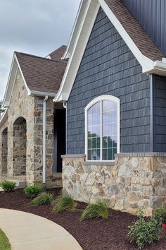 a blue house with white trim and windows on the front, along side a flower bed