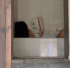 a woman laying in a bathtub reading a book