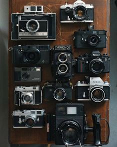 many old cameras are arranged on a wooden table with one camera attached to the wall