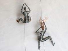 two wire sculptures are hanging on the wall, one has a plant in its hand